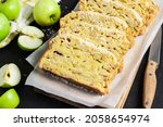 Small photo of Sliced apple and coconut oaf cake on wooden cutting board on dark background