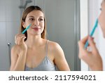 Small photo of Beautiful young woman shaving her face by razor at home. Pretty woman using razor on bathroom.