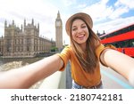 Smiling tourist girl taking self portrait in London, UK. Selfie photo of happy woman traveling in London with Big Ben tower, Westminster palace and double decker red bus on summer sunny day.