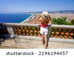 Holidays in Nice, French Riviera. Back view of beautiful girl holding hat enjoying view of the cityscape of Nice, France.