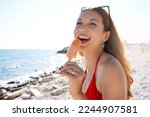 Funny Brazilian girl eating popsicle on the beach. Looking up. Copy space.