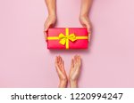 Top view of male and female hands holding red gift box with golden ribbon on pink background Flat lay. Present for birthday, valentine day, Christmas, New Year. Congratulations background copy space.