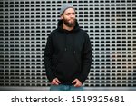 City portrait of handsome hipster guy with beard wearing black blank hoodie or sweatshirt and hat with space for your logo or design. Mockup for print