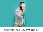 Small photo of Portrait of a man with a beard covering his face with a white mask hiding his real mysterious identity. Hypocrisy, fraud, lie and insincerity concept. Indoor studio shot against a blue background.