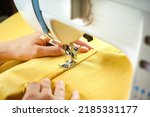 Seamstress female hands holding and stitching yellow textile fabric on modern sewing machine at workplace. Sewing process, upholstery, clothes, repair, DIY. Handmade, hobby, small business concept