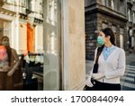 Woman with mask looking at a closed fashion clothes storefront.Clothing shopping during coronavirus outbreak shutdown.COVID-19 quarantine apparel retail store closures.Small business loss concept.