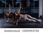Small photo of Two beautiful women with athletic figures perform a side bar in a dark gym. Two female athletes make balance from yoga.