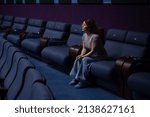 Caucasian red-haired woman sits on the last row in a cinema in an empty hall. The girl is watching a movie alone.