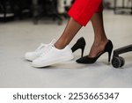 African woman changing from high heels to sneakers in the office. Tired legs. 