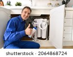 Small photo of Technician installing reverse osmosis equipment under the sink with ok sign. Front view. Horizontal composition.