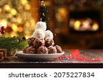Pile of coconut and chocolate balls on Christmas with grated coconut shavings falling on top and homey background with a Christmas tree with lights and fireplace burning. Front view.