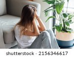Small photo of Unhappy young caucasian woman with blonde hair thinking about bad relationships problems, break up with boyfriend. Worried millennial girl sitting on floor in bedroom near chair and green plant alone