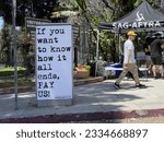 Small photo of LOS ANGELES, July 18th, 2023: Writers strike. Actors strike. WGA. SAG-AFTRA.Man walks past strike tent next to large protest sign on the picket lines at 20th Century Fox Studios, Century City.