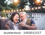 Happy senior couple having fun at dinner house party - Older people with different ethnicity doing a romantic date for celebrating anniversary - Elderly, food, drink and love concept