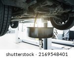 Small photo of Engine oil change in car service. Auto is on hydraulic lift in garage workshop, process of draining old dark used oil