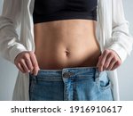 Small photo of A slender woman with a bare stomach shows how she lost weight. Jeans have become too big. The concept of diet and healthy eating