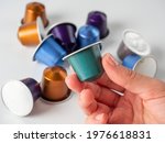 colored aluminum capsule with ground coffee in hand. White background with other capsules lying on it. Modern methods of making coffee. Capsule for coffee machine