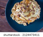 Small photo of Sweet delicious dessert a cinnamon bun sprinkled with pecans and poured with caramel topping on a black plate and a turd background. Top view flat lay