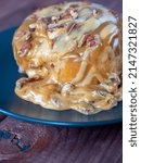 Small photo of Sweet delicious dessert a cinnamon bun sprinkled with pecans and poured with caramel topping on a black plate and a turd background. vertical photo