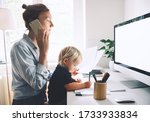 Small photo of Modern mom balances between work and child home schooling on sick leave or quarantine. Mother works from home with kid. Woman responding on phone calls, working on computer with a toddler on her lap.