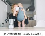 Modern young tired mom and little child after sleepless night. Exhausted woman with baby is sitting with coffee in kitchen. Life of working mother with baby. Postpartum depression on maternity leave.