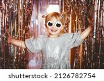 Happy little stylish girl in shiny dress having fun. Festive background with foil curtain decorations for kids birthday or fancy dress party, disco music or New Year. Celebration and Holiday concept.