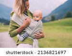 Small photo of Babywearing. Mother and baby on nature outdoors. Baby in wrap carrier. Woman carrying little child in baby sling in green mint color. Concept of green parenting, natural motherhood, postpartum period.