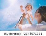 Mother throwing baby up against the blue sky. Happy family outdoors. Mom and baby at summer on nature. Positive human emotions and feelings.