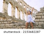 Сute little girl with family exploring Roman Amphitheater Arena like as Coliseum - famous tourist travel destination in Pula, Croatia. A child plays in historical ruins of an ancient structure