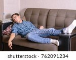 Small photo of The sleeping young man on the couch in the room, tired after work, drunk after a party. Fell asleep anyhow