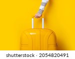 Female hand holds a yellow suitcase on a bright yellow background