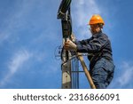 Small photo of A technician working on ladder carefully for maintenance fiber optic wires attached to electric poles. Safety equipment and Operational safety.