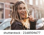 Small photo of Pensive blonde woman in black leather jacket put off black glasses and turn around posing on street background. Outdoor shot of happy hippie lady with two thin braids and wave hair. Boho freedom style