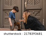 Small photo of Mother scolds her son on the street. A child cries, a woman shakes her finger because of the boy bad behavior, while walking to home. Rule of conduct. Woman sitting, boy cover his face and cry.