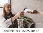 Small photo of Blonde attractive woman paying with cellphone resting in cafe while waitress holding payment terminal. Girl relaxing in restaurant. Focus on part payment terminal and mobile phone.