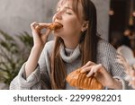 Small photo of Young blonde woman with bang eating croissants at a cafe. Girl bite piece of croissant look joyful at restaurant. Cheat meal day concept. Woman is preparing with appetite to eat croissant.