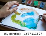 Small photo of Child's drawing of watercolor paints in a sketch notebook, children's creativity concept. Child's hands next to the picture. Monotype. Drawing of an unusual fairytale animal.
