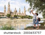 Young family playing with their baby at the Ebro river bank with Basilica del Pilar on the background. Family vacation in Zaragoza, Spain.