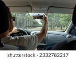 View of a blurred man adjusting rear view mirror while driving on a road through pine forest.