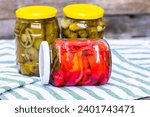 Small photo of Glass jars with pickled red bell peppers and pickled cucumbers (pickles) isolated. Jars with variety of pickled vegetables. Preserved food concept in a rustic composition.