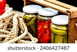Small photo of Wooden crate with glass jars with pickled red bell peppers and pickled cucumbers (pickles) isolated. Jars with variety of pickled vegetables. Preserved food concept in a rustic composition.