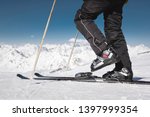 Close-up of the athlete's skier's foot in ski boots rises into the skis against the background of the snow-capped Caucasus mountains on a sunny day. Winter sports concept