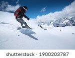 Young woman snowboarder in deep snow - extreme freeride on the background of snow-capped mountains on a sunny day