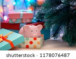 Under a Christmas tree in a holiday box we lay a piggy bank. A gift, a symbol of the new year. An unusual photo.