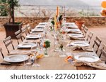 Table decor for a festive lunch or al fresco dinner in orange, yellow and green. The table is decorated with flowers and candles.

