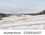 Agricultural field with dry grass covered with first snow. Cloudy day in late autumn. Nature landscape background