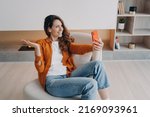 Homey caucasian girl has video phone call. Relaxed young woman is using airpods and cellphone at home. Wireless earphones using at online meeting. Technology using, leisure and communication concept.