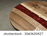 Small photo of Expensive vintage furniture. The table is covered with epoxy resin and varnished. Luxury quality wood processing. Reflections of light in polished varnish. A red epoxy river in a round tree slab.