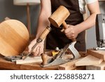 Closeup portrait of unknown faceless man master wearing brown apron using mallet and chisel for making wooden furniture, craftsman working in his joinery workshop.