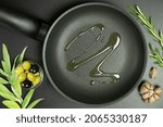 Top view of frying pan with olive oil and ingredients around it on dark background. Concept of healthy plant food. Flat lay, layout.